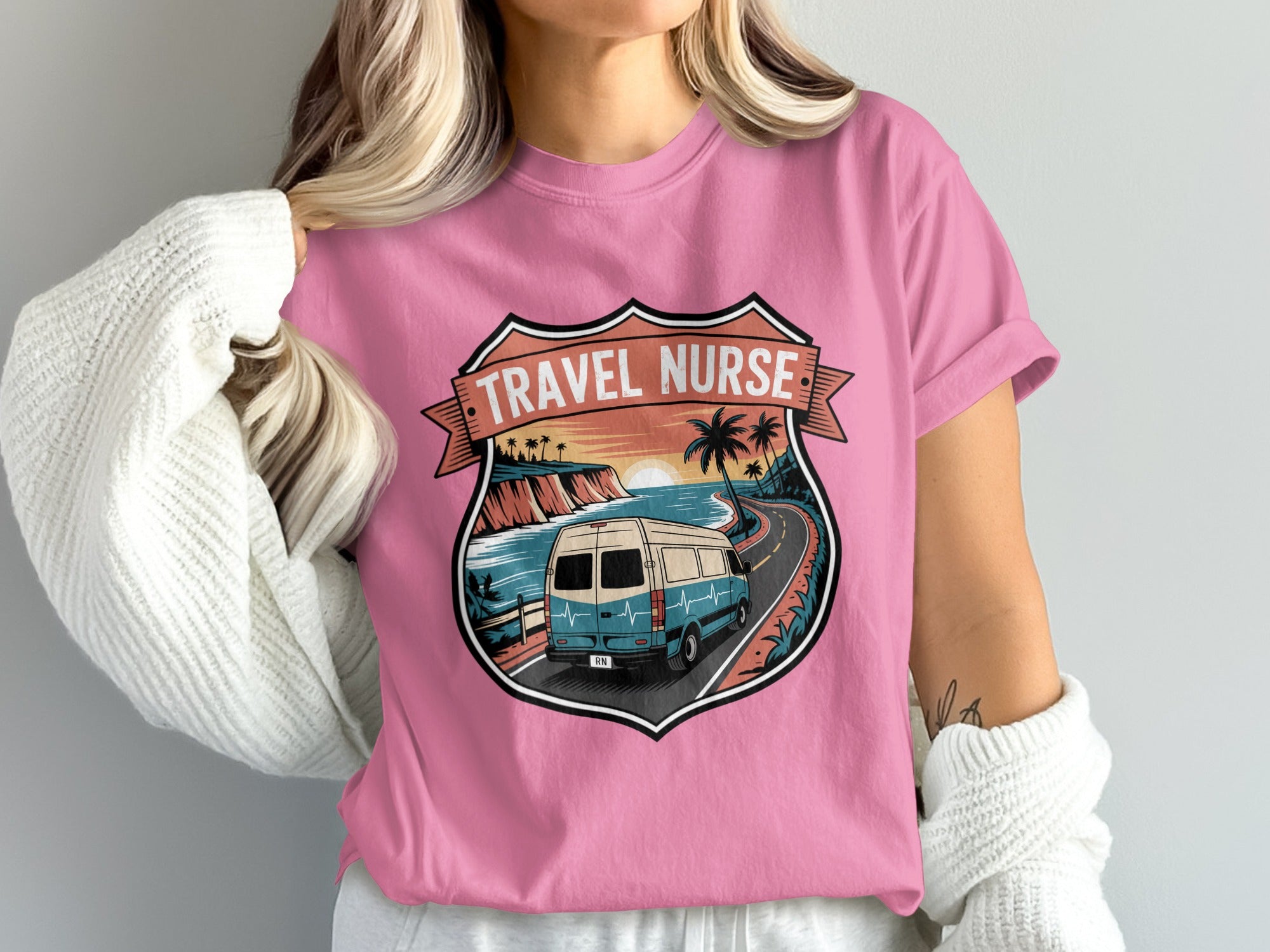 Pink t-shirt featuring a shield graphic with a van driving on a coastal road.