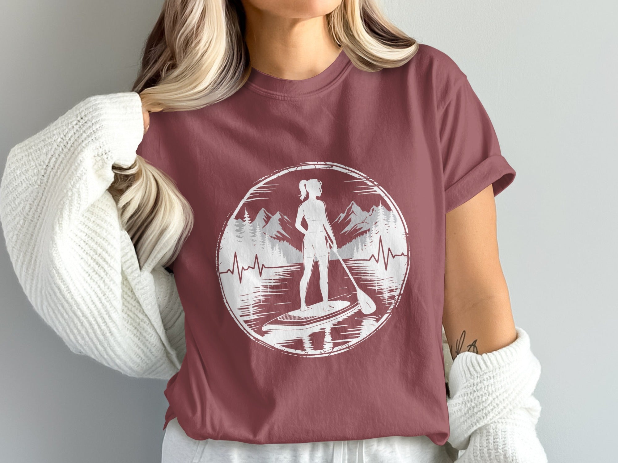 Maroon t-shirt with a graphic of a woman paddleboarding against a mountain and heartbeat line.