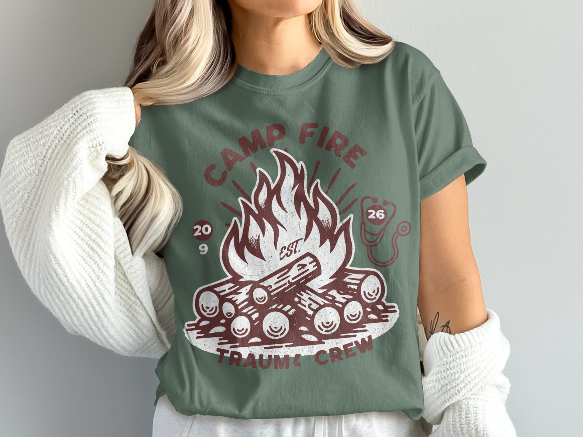 Camp Fire Trauma Crew design on a green t-shirt with a stethoscope icon.