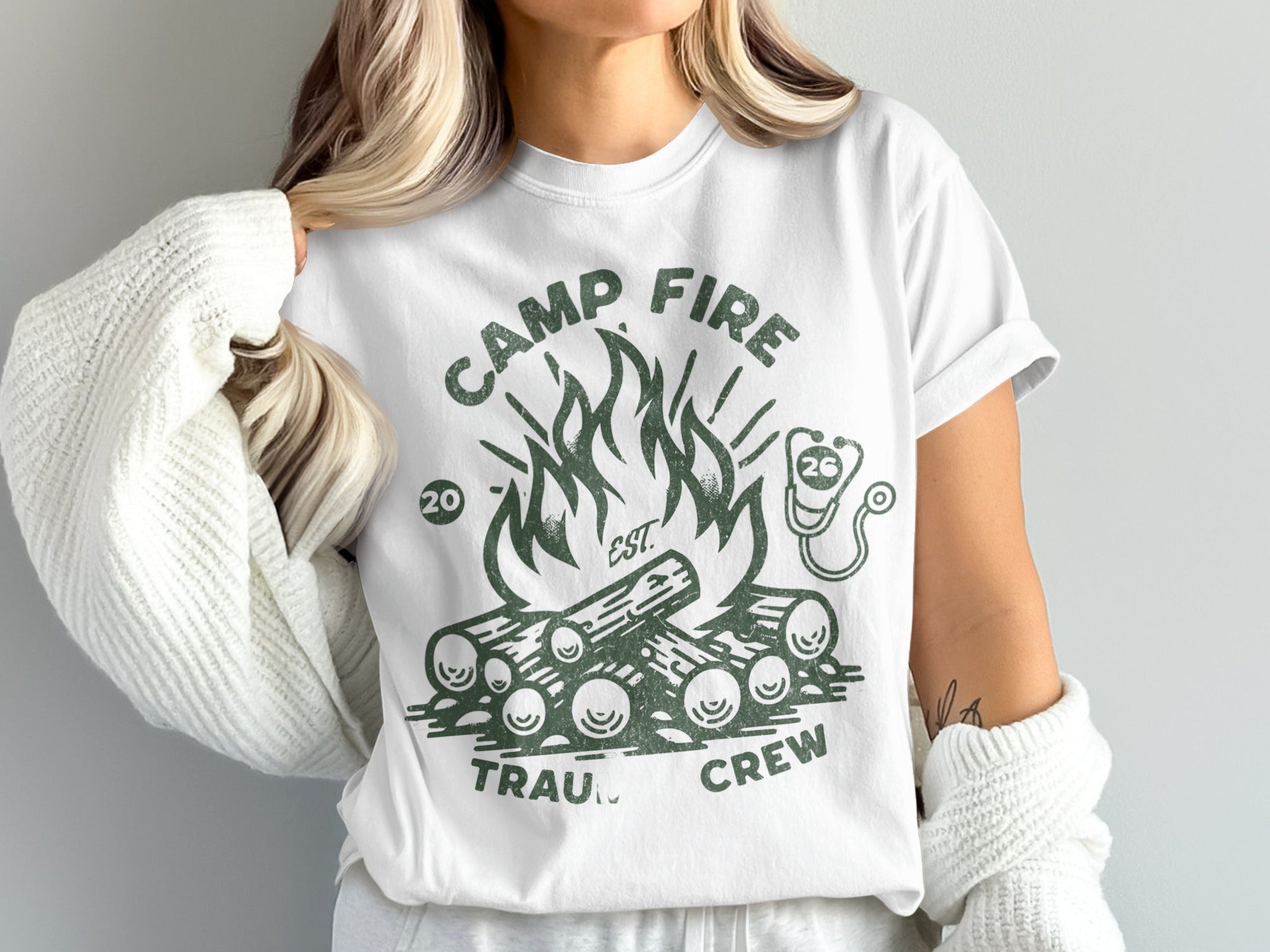 White t-shirt with green graphic of campfire and "Camp Fire Trauma Crew" text.
