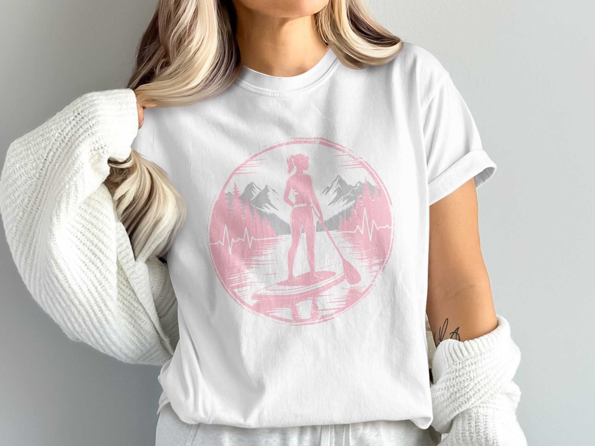 White t-shirt with a pink circular graphic of a paddleboarder against mountains and a heartbeat line.