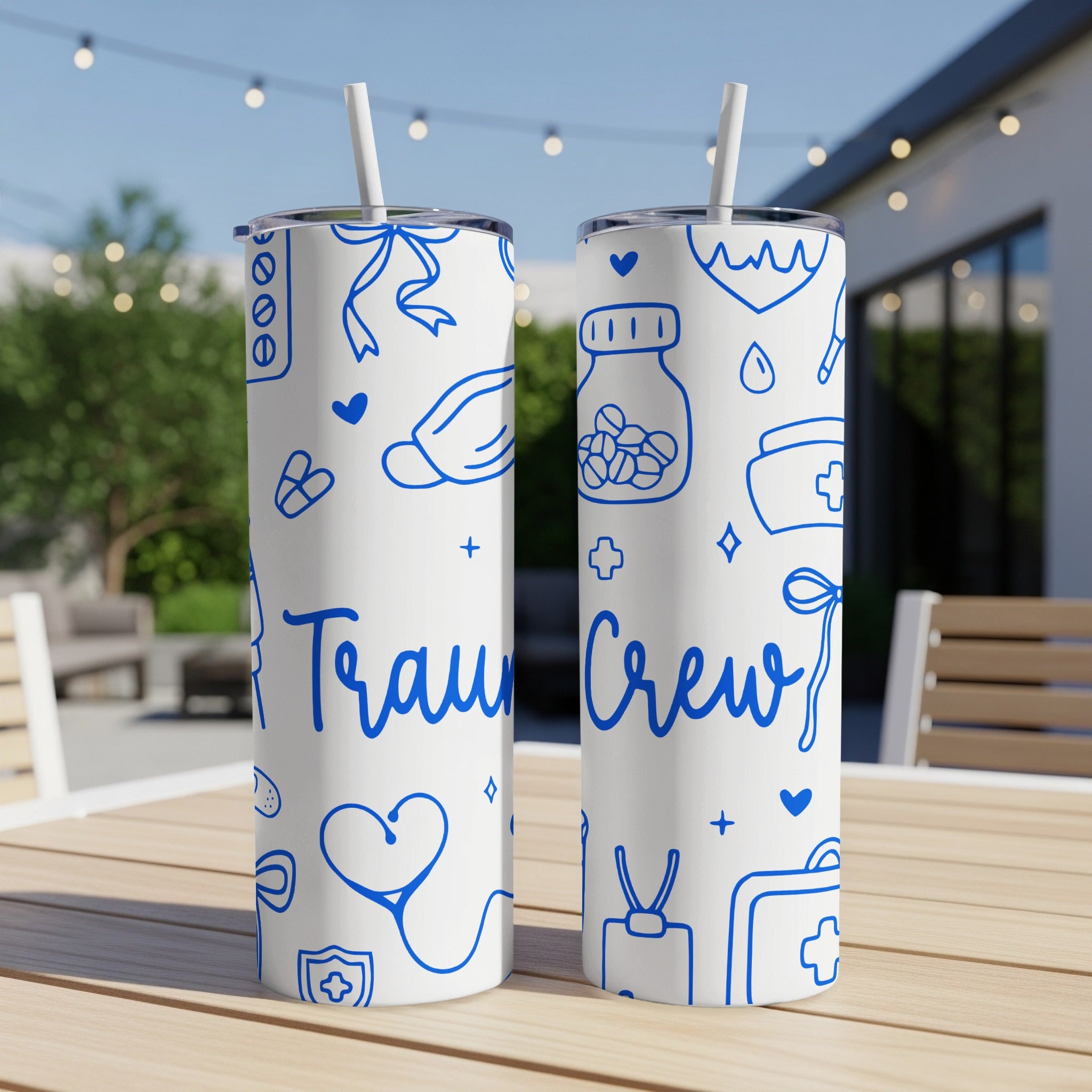 Two blue and white "Trauma Crew" tumblers with medical icons on a patio table.