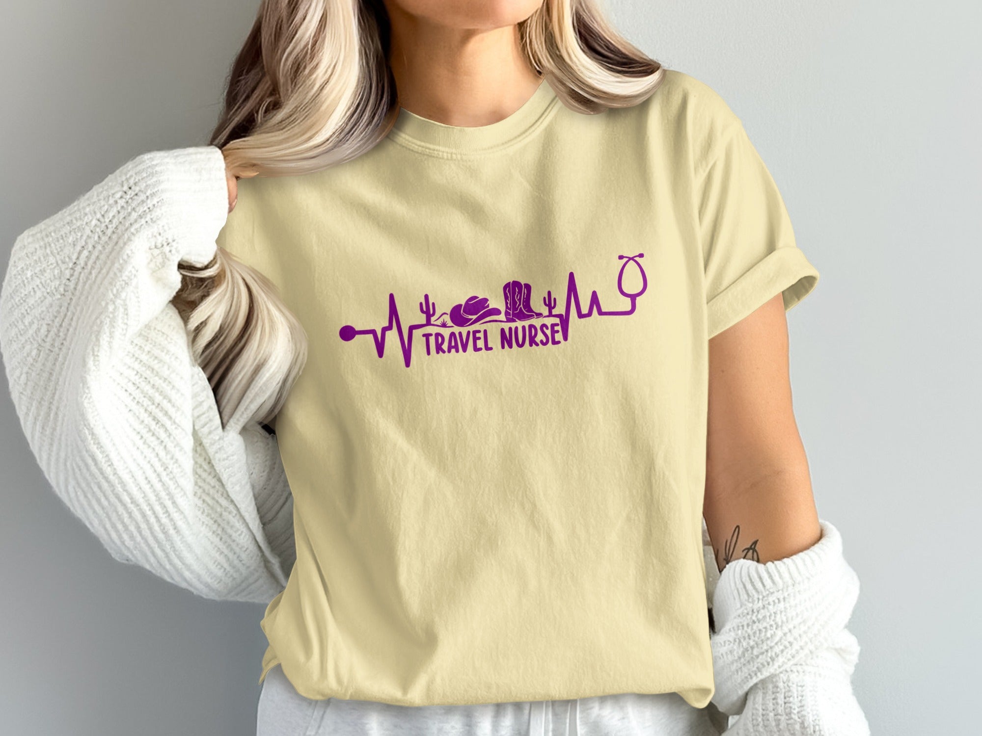 Cream t-shirt with purple heartbeat line featuring travel and medical symbols.