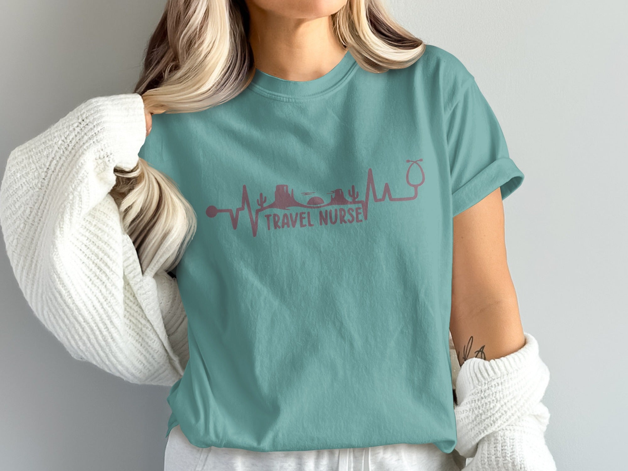 Teal t-shirt with a stethoscope heart monitor line featuring travel icons.