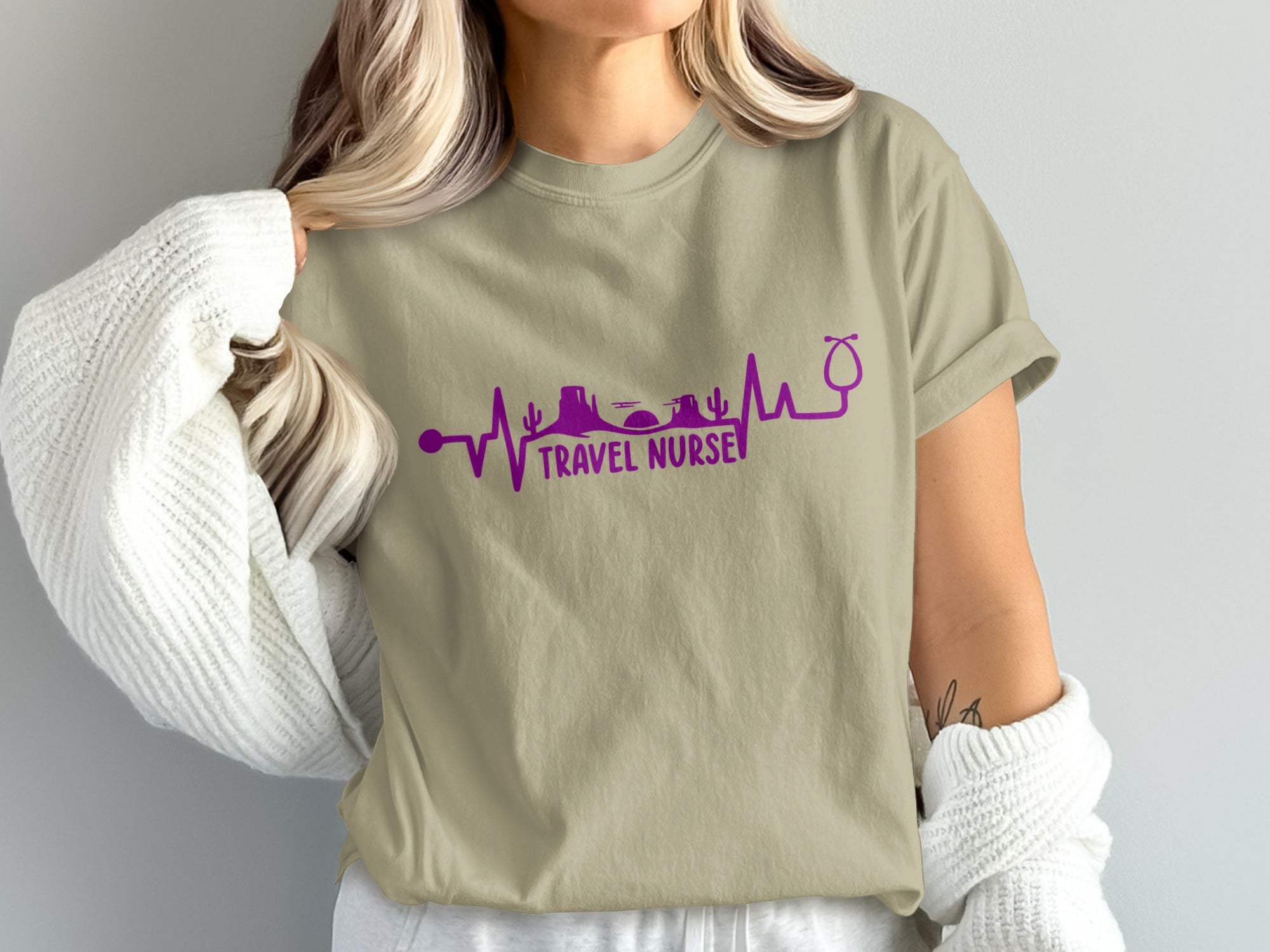 Beige t-shirt with "TRAVEL NURSE" in purple, featuring a heartbeat line with desert landscape and stethoscope.