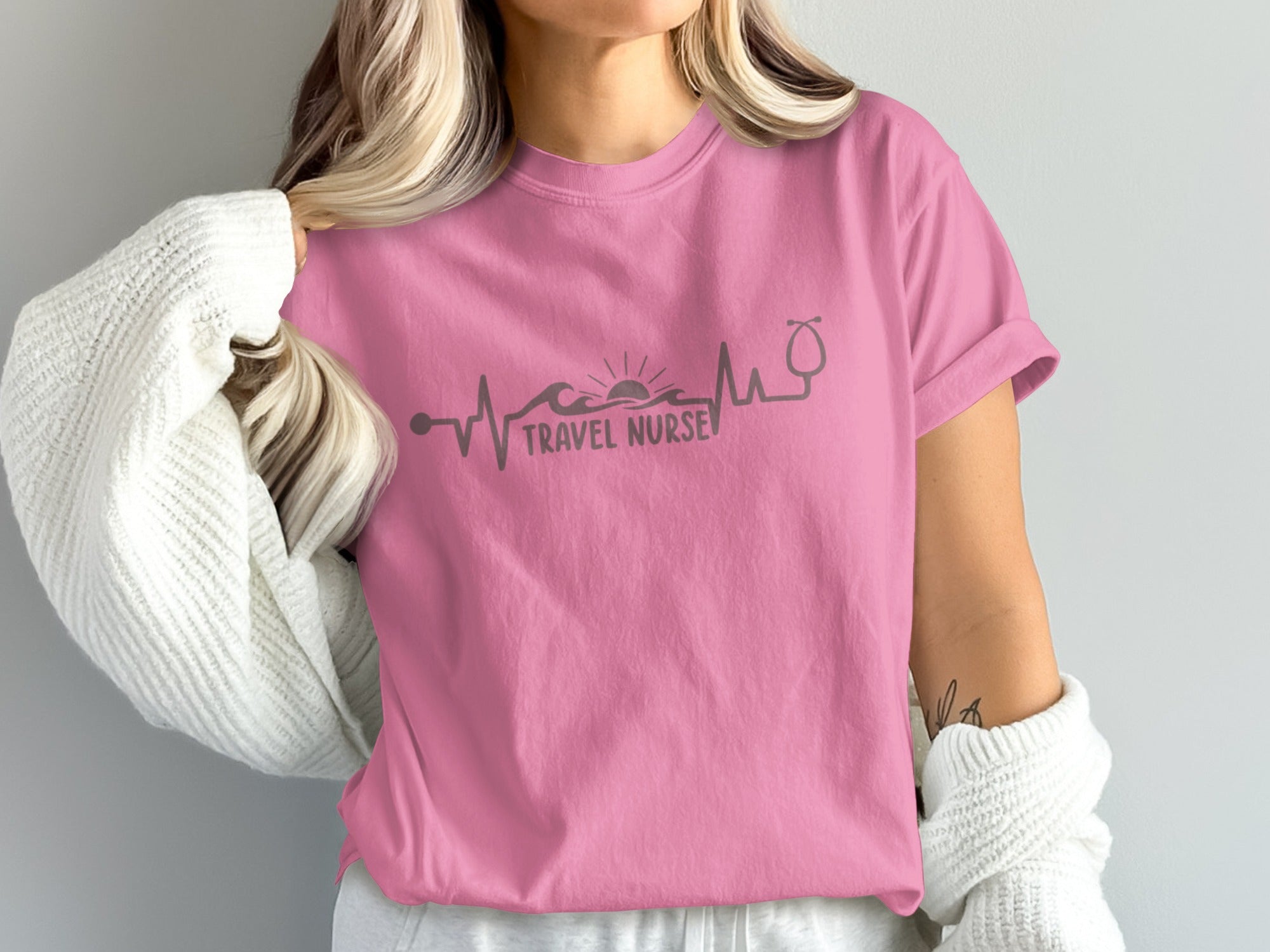 Pink t-shirt with a graphic of a heartbeat line, sun, waves, and stethoscope.