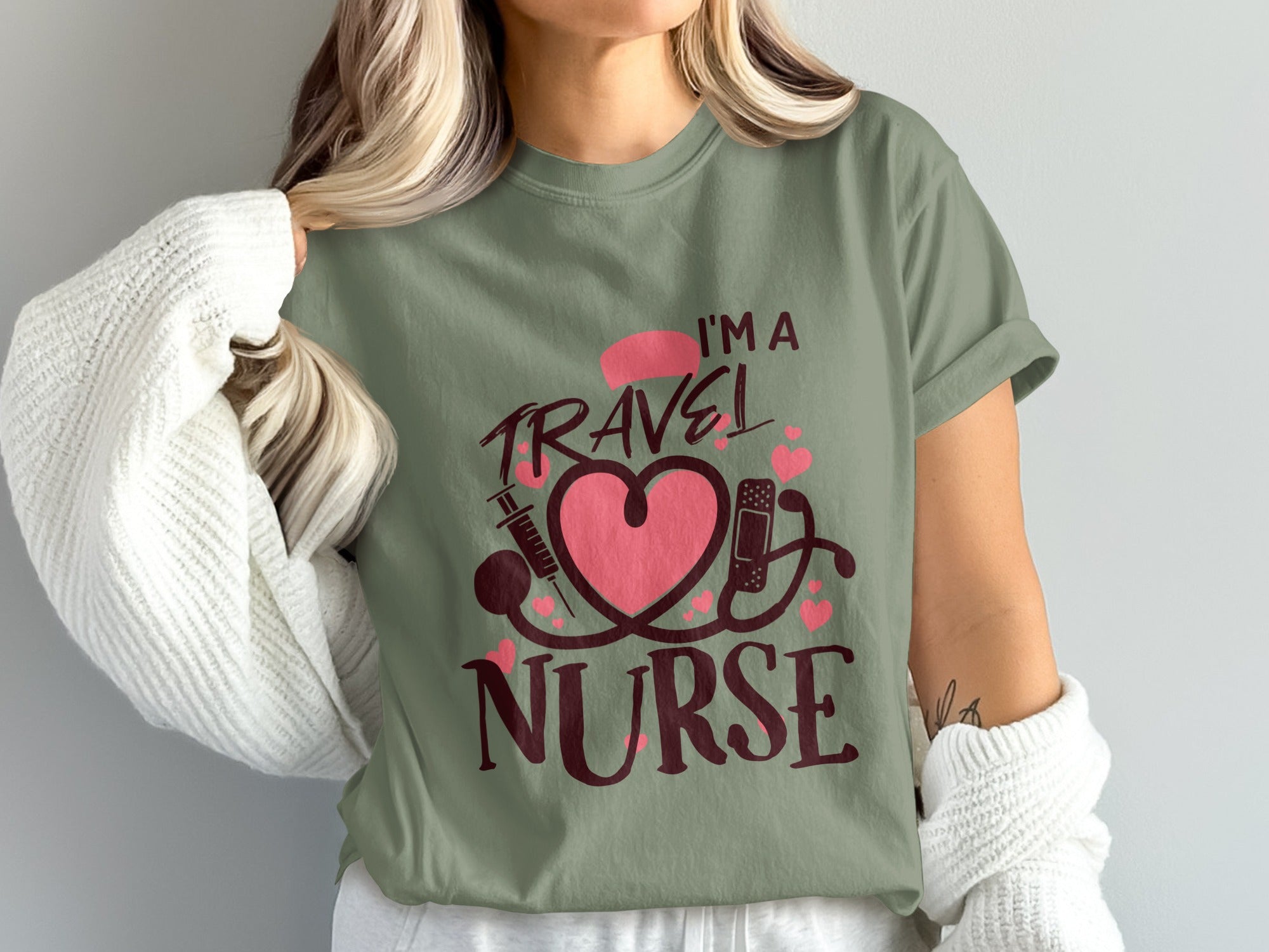 Olive green t-shirt with "I'M A TRAVEL NURSE" text, heart, syringe, and stethoscope graphics.