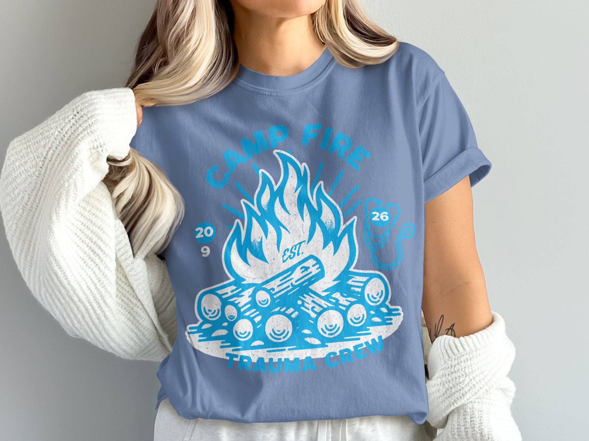 Blue t-shirt with white graphic of campfire and "Camp Fire Trauma Crew" text.