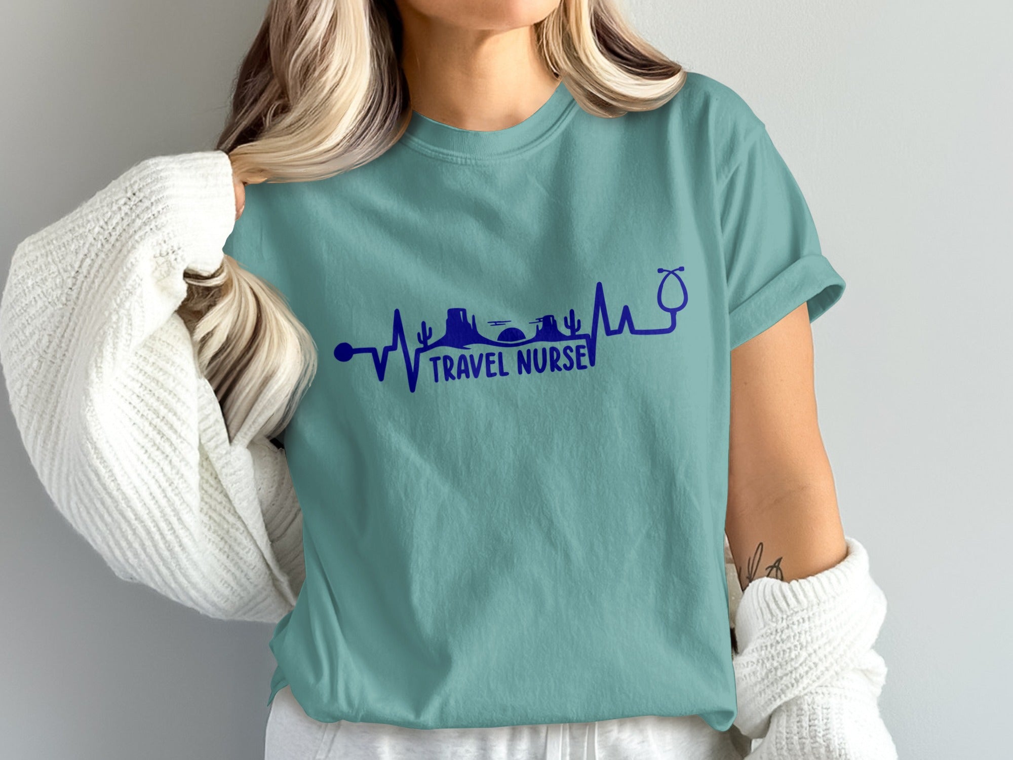 Teal t-shirt with a heartbeat line graphic, mountains, and stethoscope, reading "Travel Nurse."