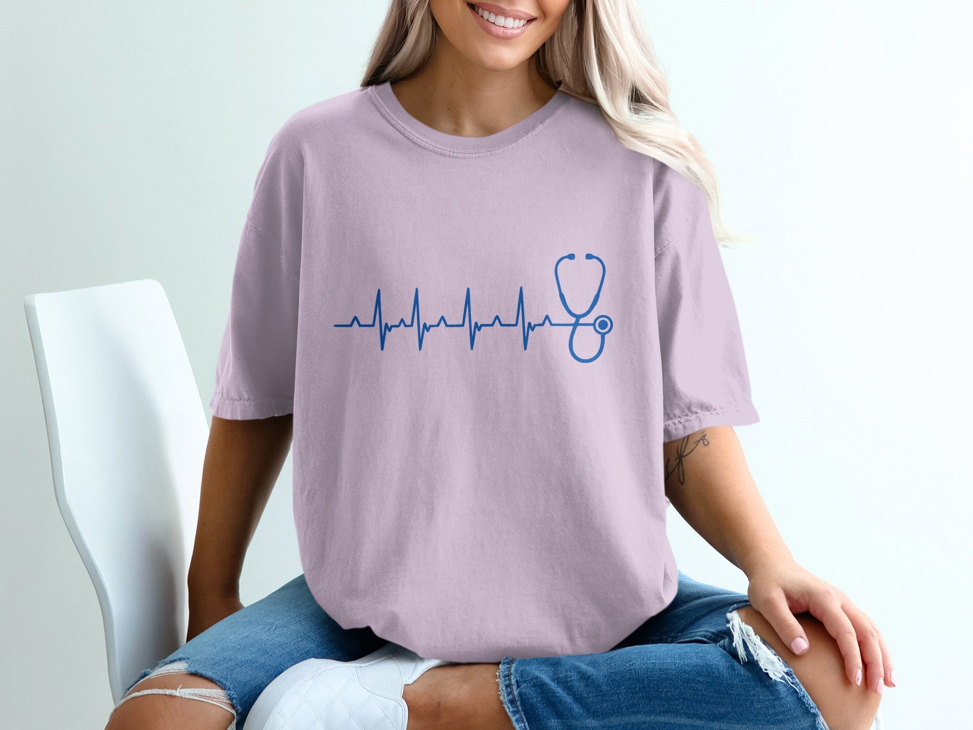 Woman wearing a light purple t-shirt with a blue stethoscope electrocardiogram graphic.