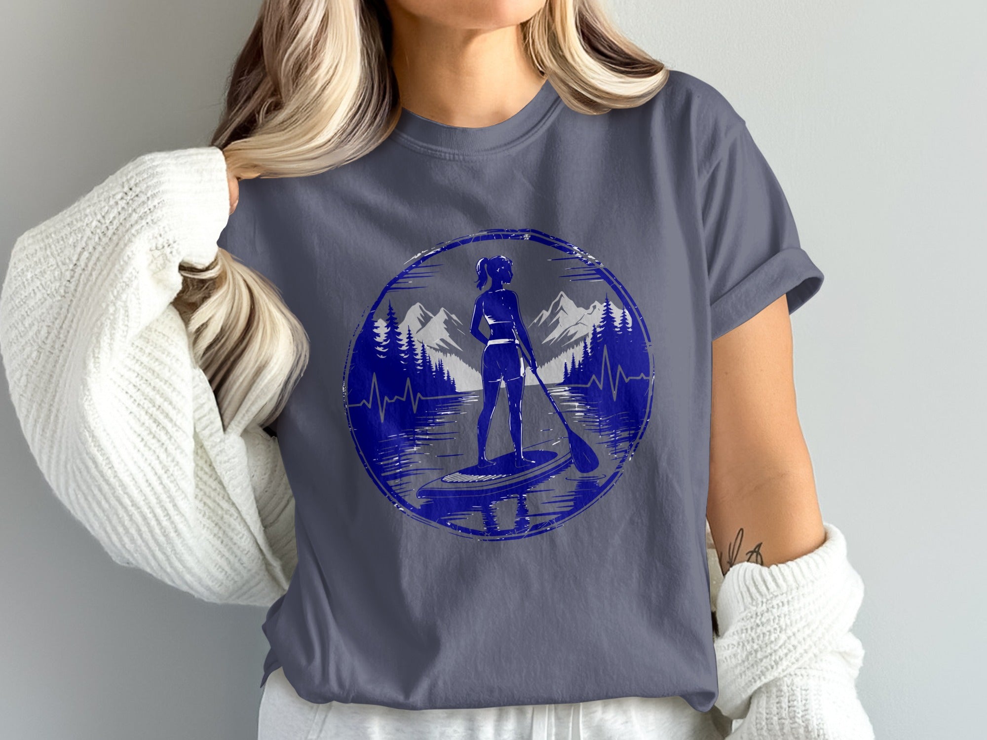 Woman paddleboarding in a circular mountain and lake graphic on a navy t-shirt.