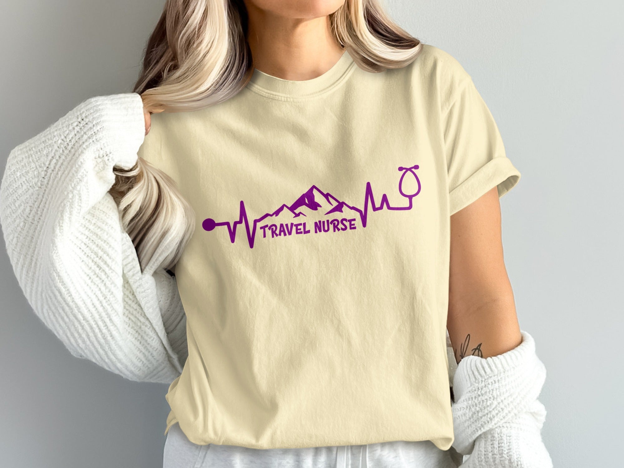 Cream t-shirt with purple travel nurse heartbeat and stethoscope graphic.