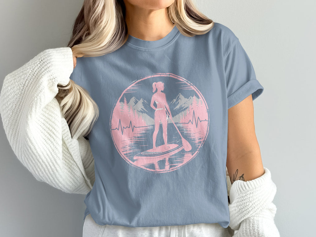 Pink silhouette of a woman paddleboarding with mountains in background.