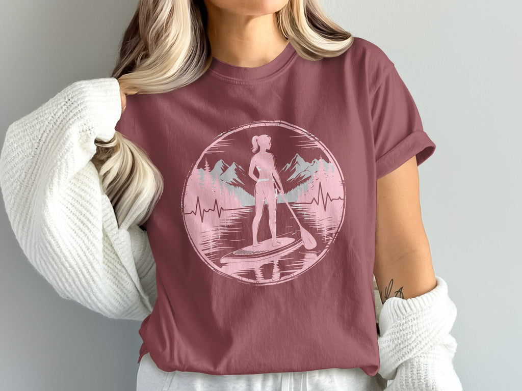 Woman paddleboarding with mountains and trees in a pink circle graphic.