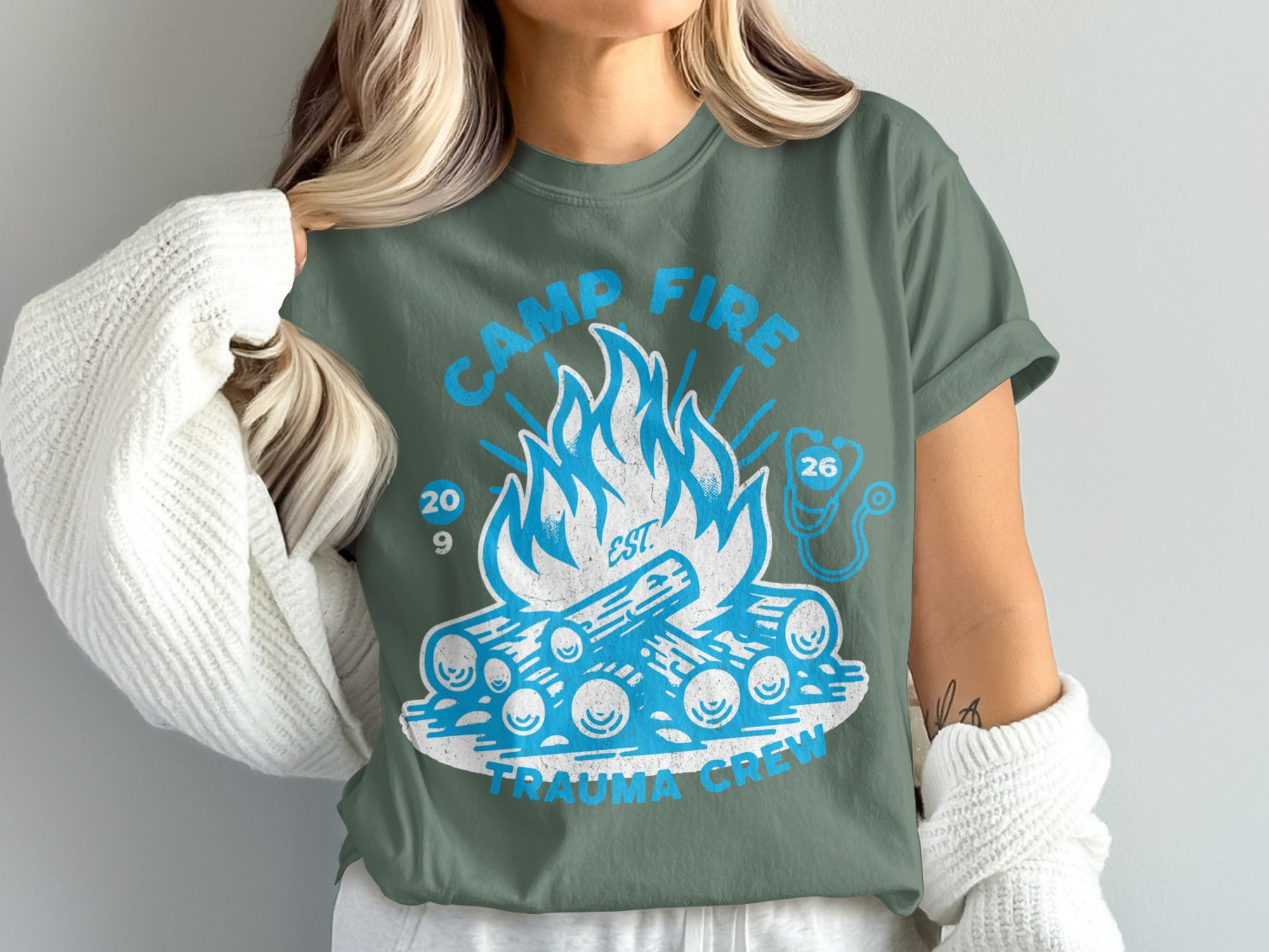 Camp Fire Trauma Crew 2026 blue graphic on green t-shirt.