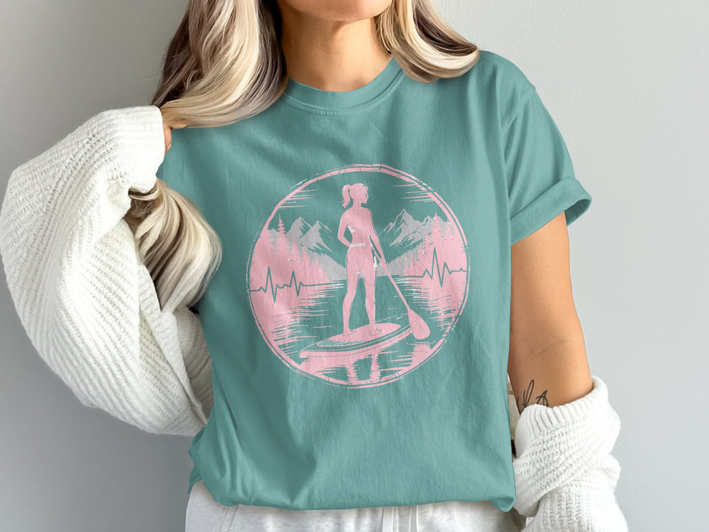 Pink silhouette of woman paddleboarding in circle with mountains.