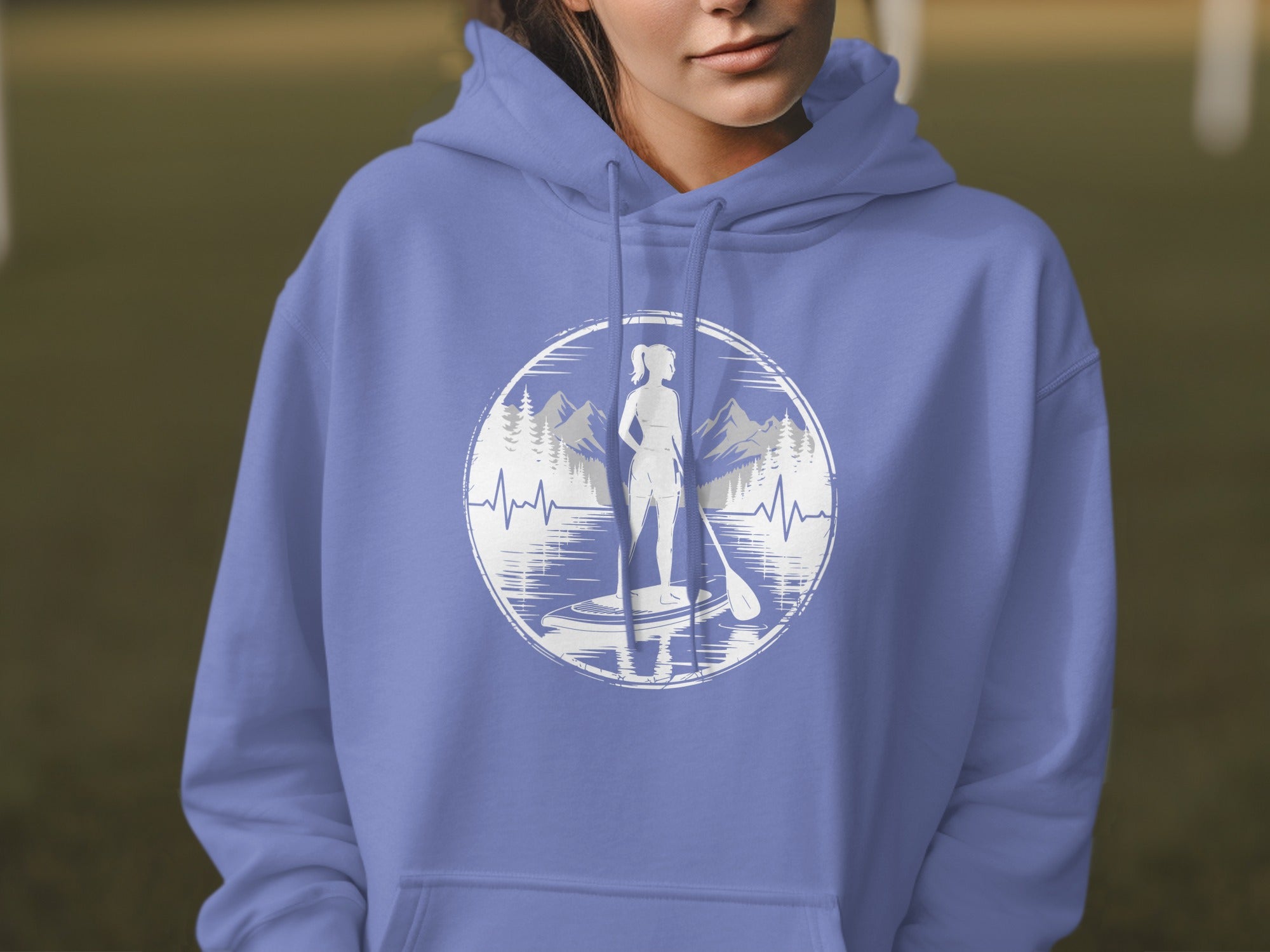 Periwinkle hoodie with circular graphic of woman paddleboarding by mountains.