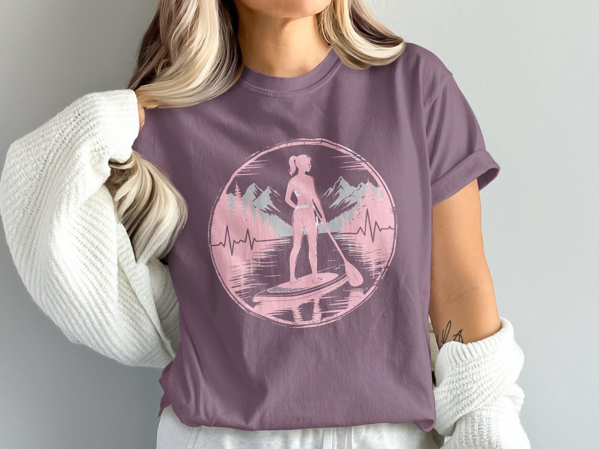Woman in purple t-shirt with paddleboarder silhouette and mountain landscape graphic.