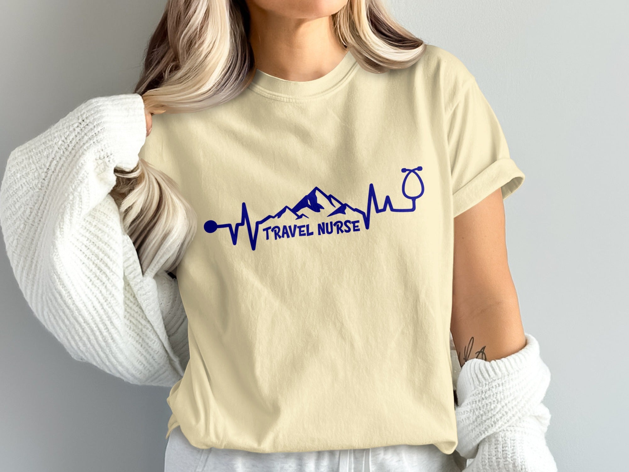 Cream t-shirt with blue "TRAVEL NURSE" text and stethoscope mountain heartbeat graphic.