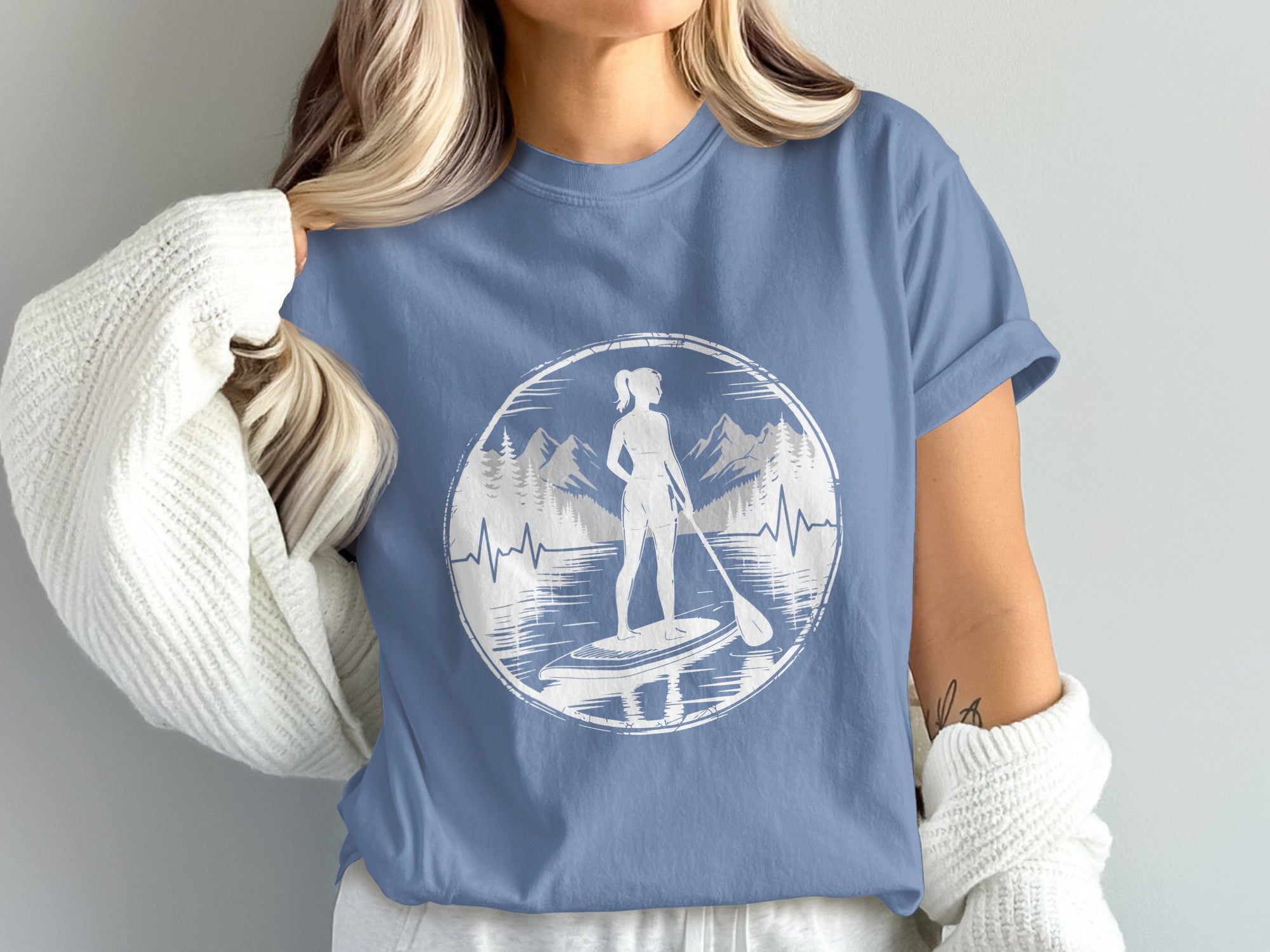 Woman wearing t-shirt with paddleboarder in mountain lake graphic.