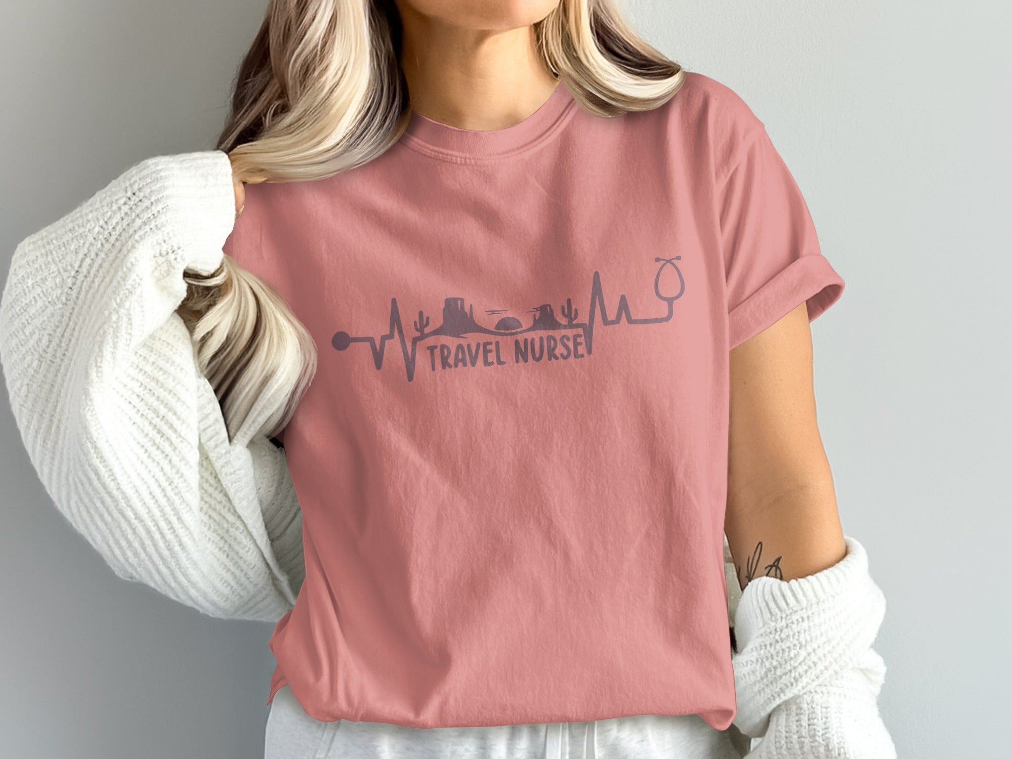 Rose-colored t-shirt with travel nurse graphic featuring heartbeat, desert, and mountains.