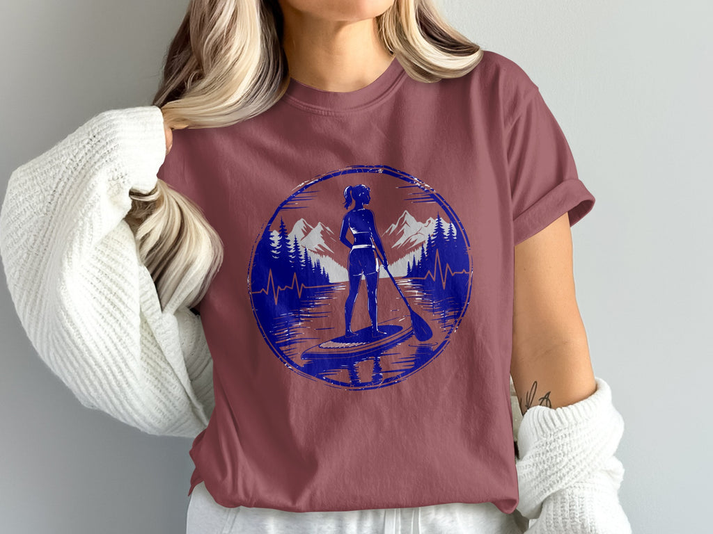 Woman on paddleboard in scenic mountain and lake landscape graphic on t-shirt.