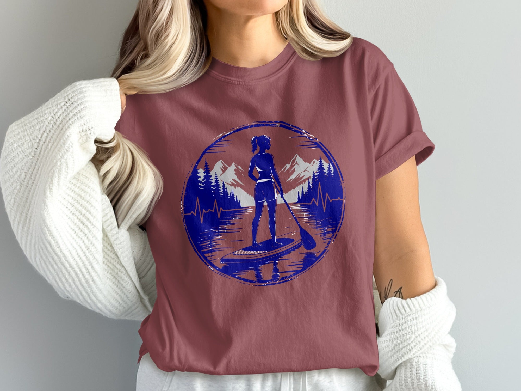 Woman on paddleboard in scenic mountain and lake landscape graphic on t-shirt.