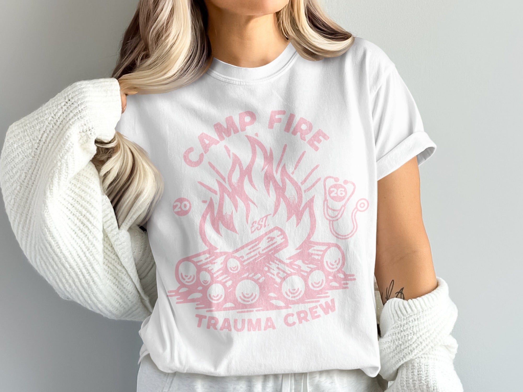 White t-shirt with pink graphic of campfire, logs, and "Camp Fire Trauma Crew" text.