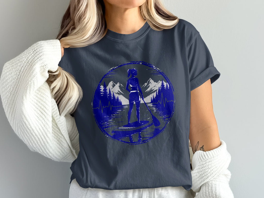 Woman in t-shirt with circular graphic of paddleboarder against mountain and lake scene.