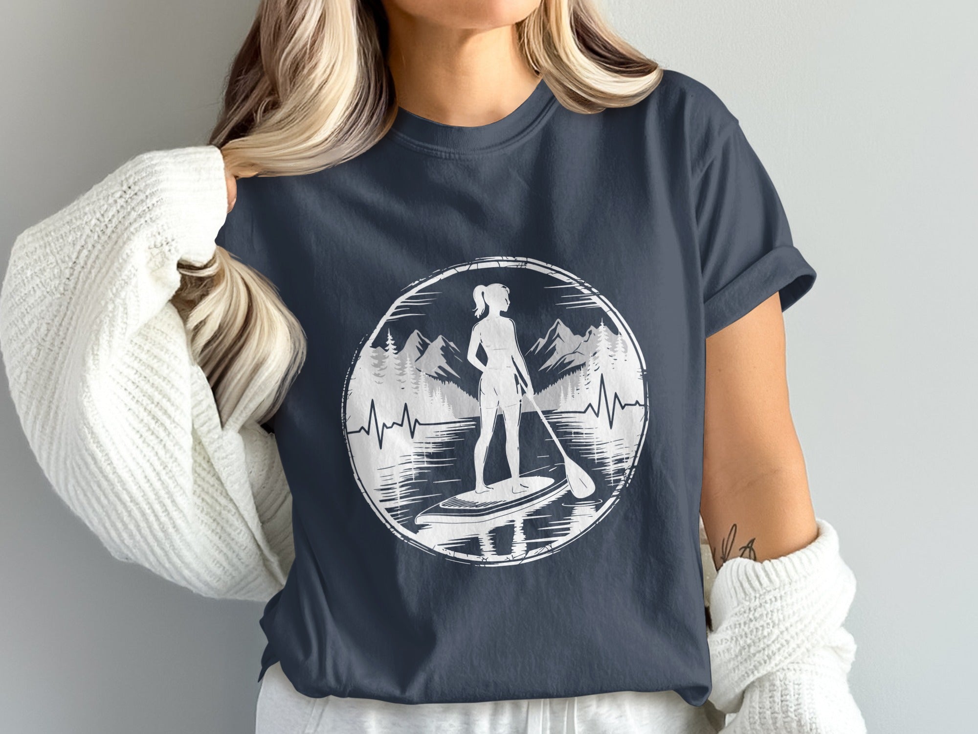 Woman wearing dark t-shirt with paddleboarder silhouette in circular nature graphic.