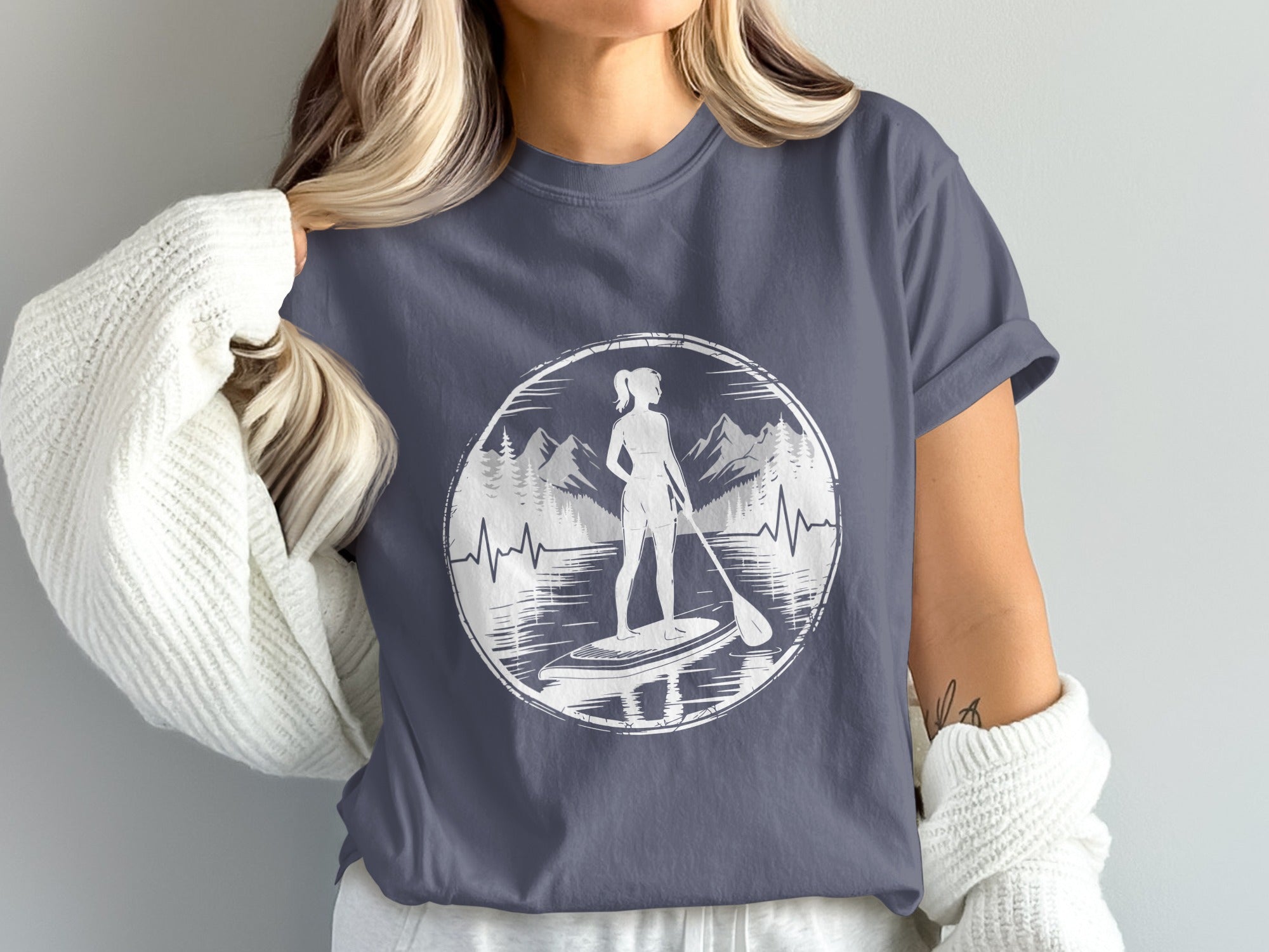 Woman wearing t-shirt with paddleboarder and mountain graphic.