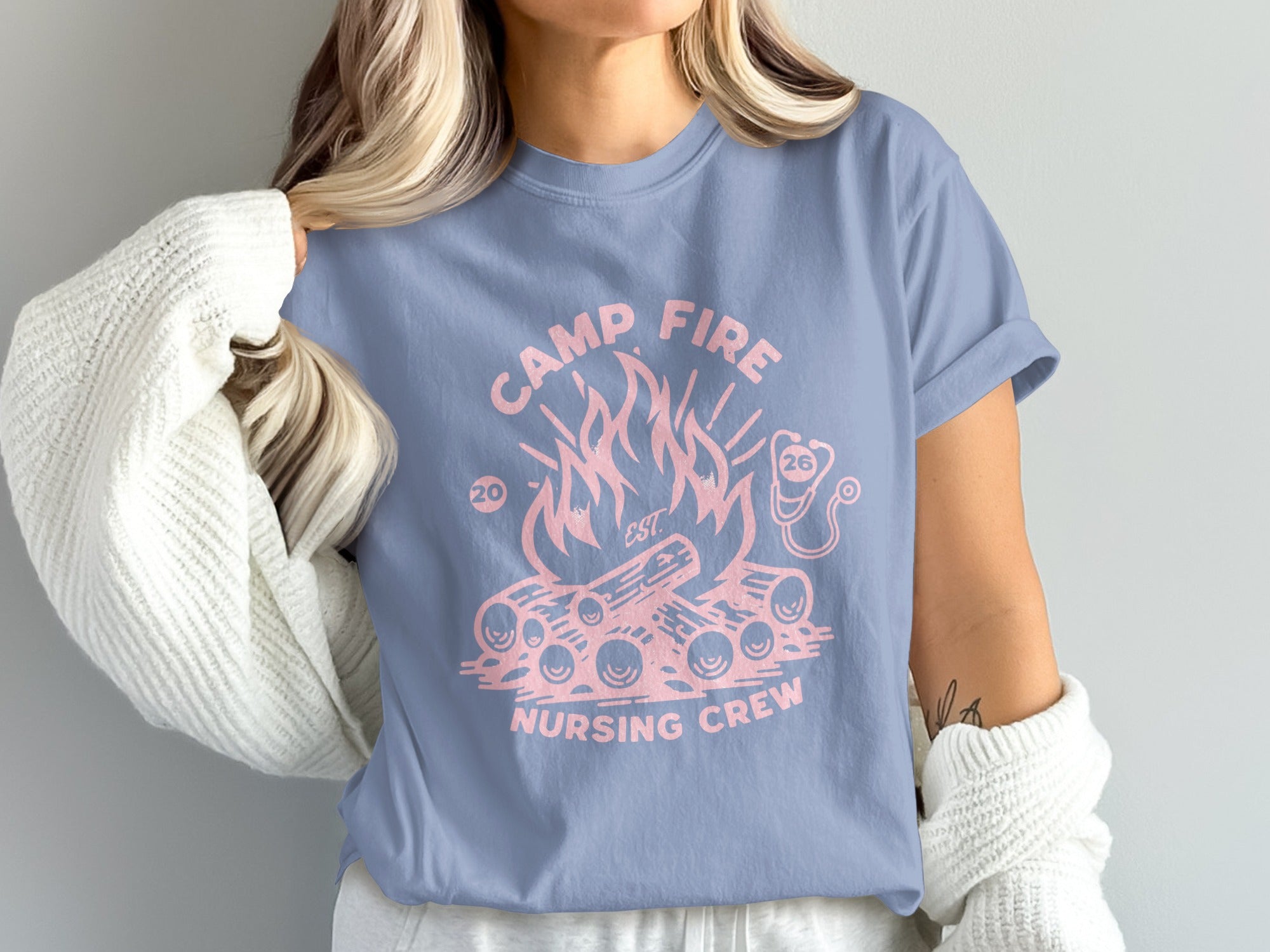 Pink campfire and wood graphic on a blue t-shirt, "Camp Fire Nursing Crew EST 2026".