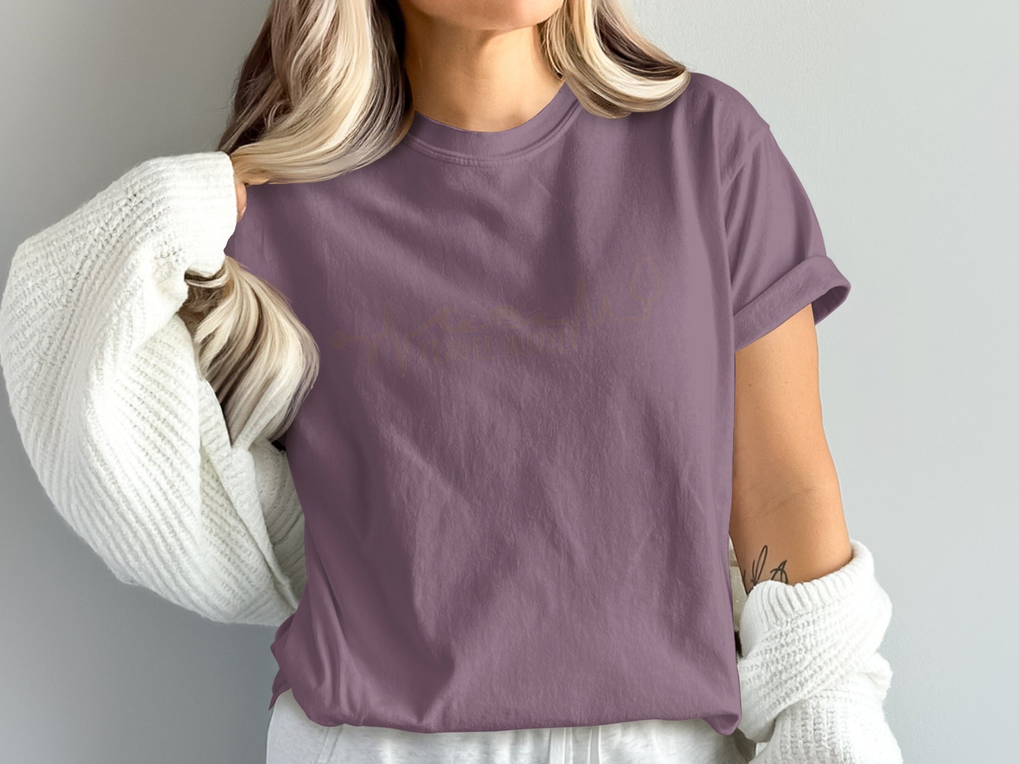 Purple t-shirt with gold cursive "Faith" graphic, worn by a person with blonde hair and white cardigan.