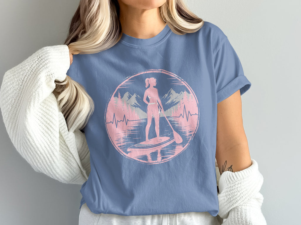 Silhouette of woman paddleboarding in a lake with mountains and trees.