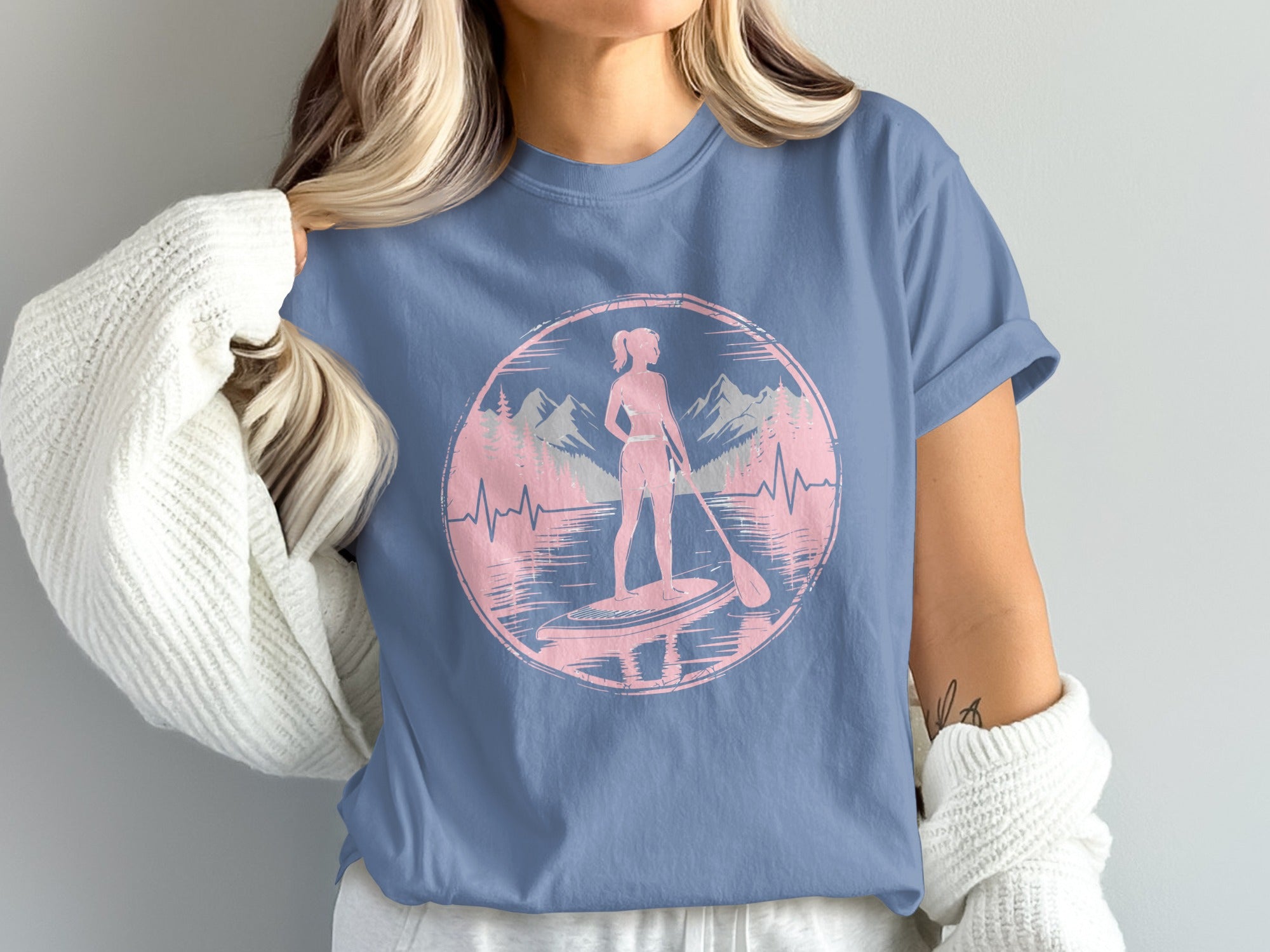 Silhouette of woman paddleboarding in a lake with mountains and trees.