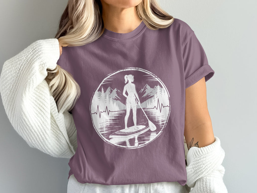 Woman wearing purple t-shirt with paddleboarder silhouette and mountain landscape graphic.