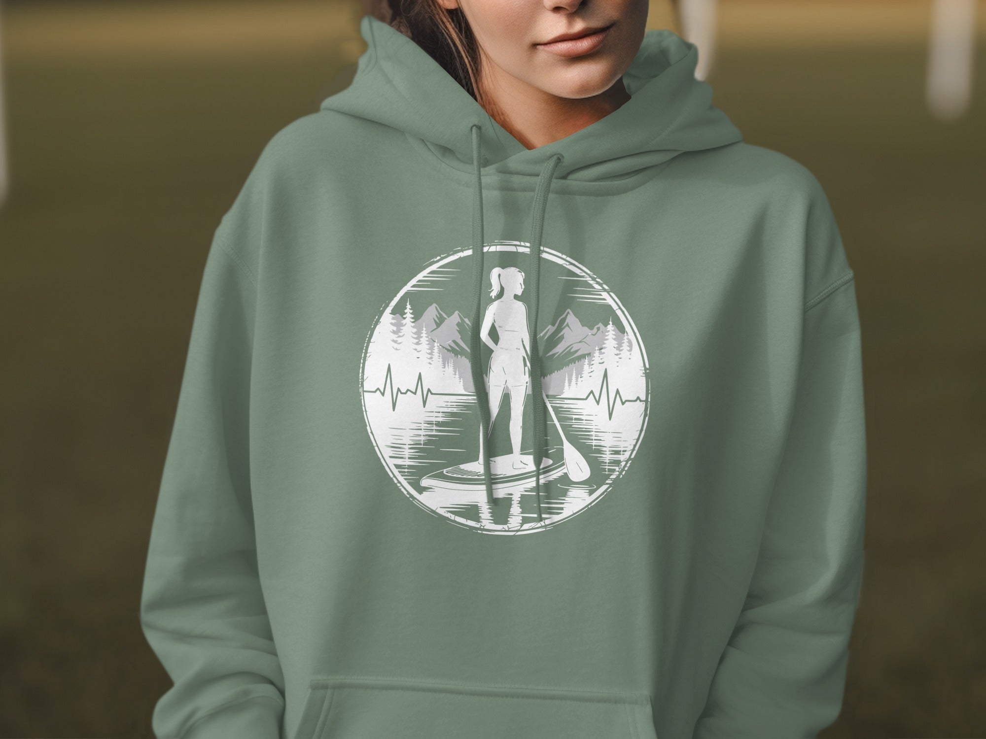 Woman in green hoodie wearing graphic tee with paddleboarder, mountains, and heartbeat.
