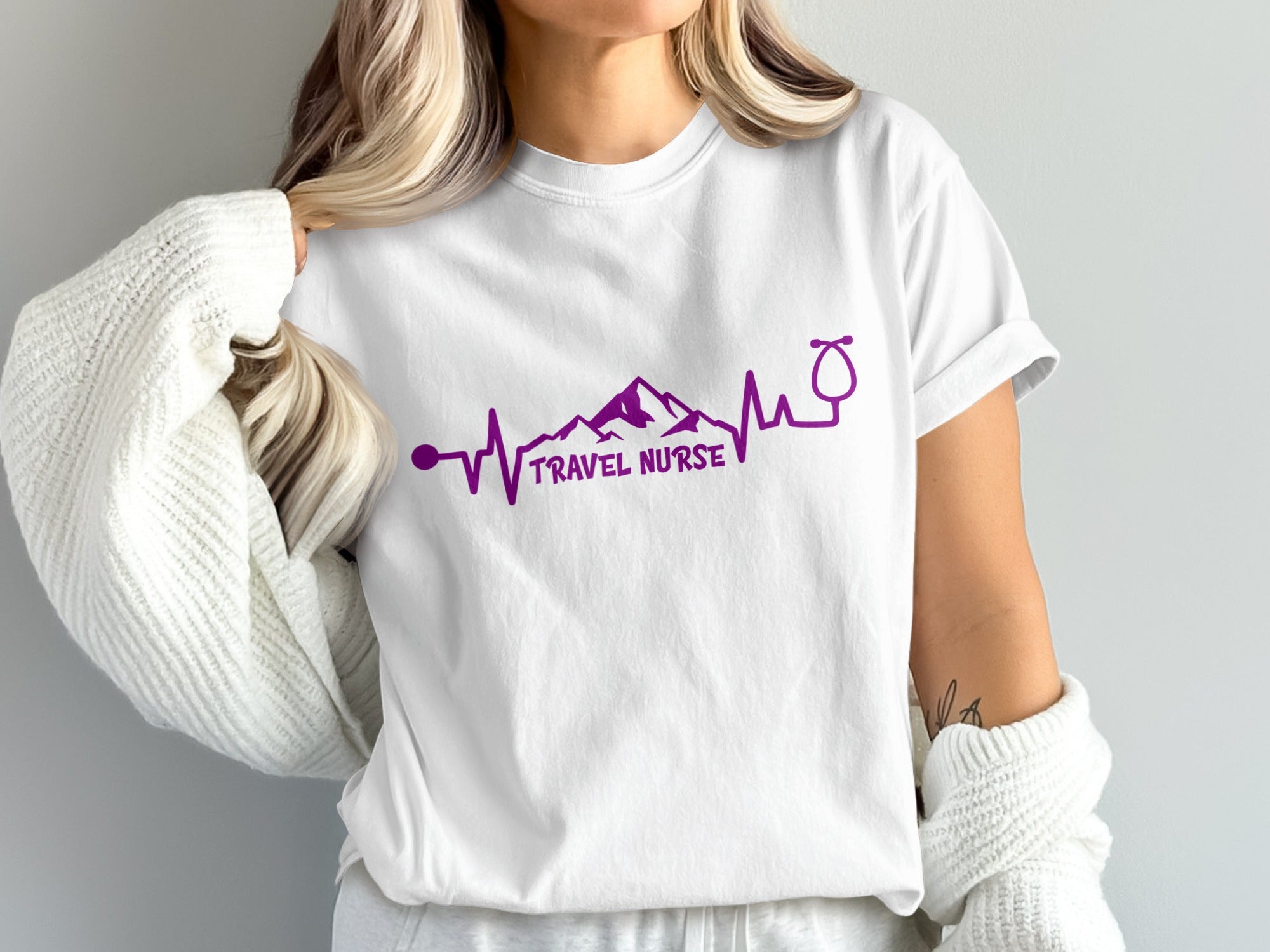 White t-shirt with purple heartbeat, mountain, and stethoscope design and "TRAVEL NURSE" text.
