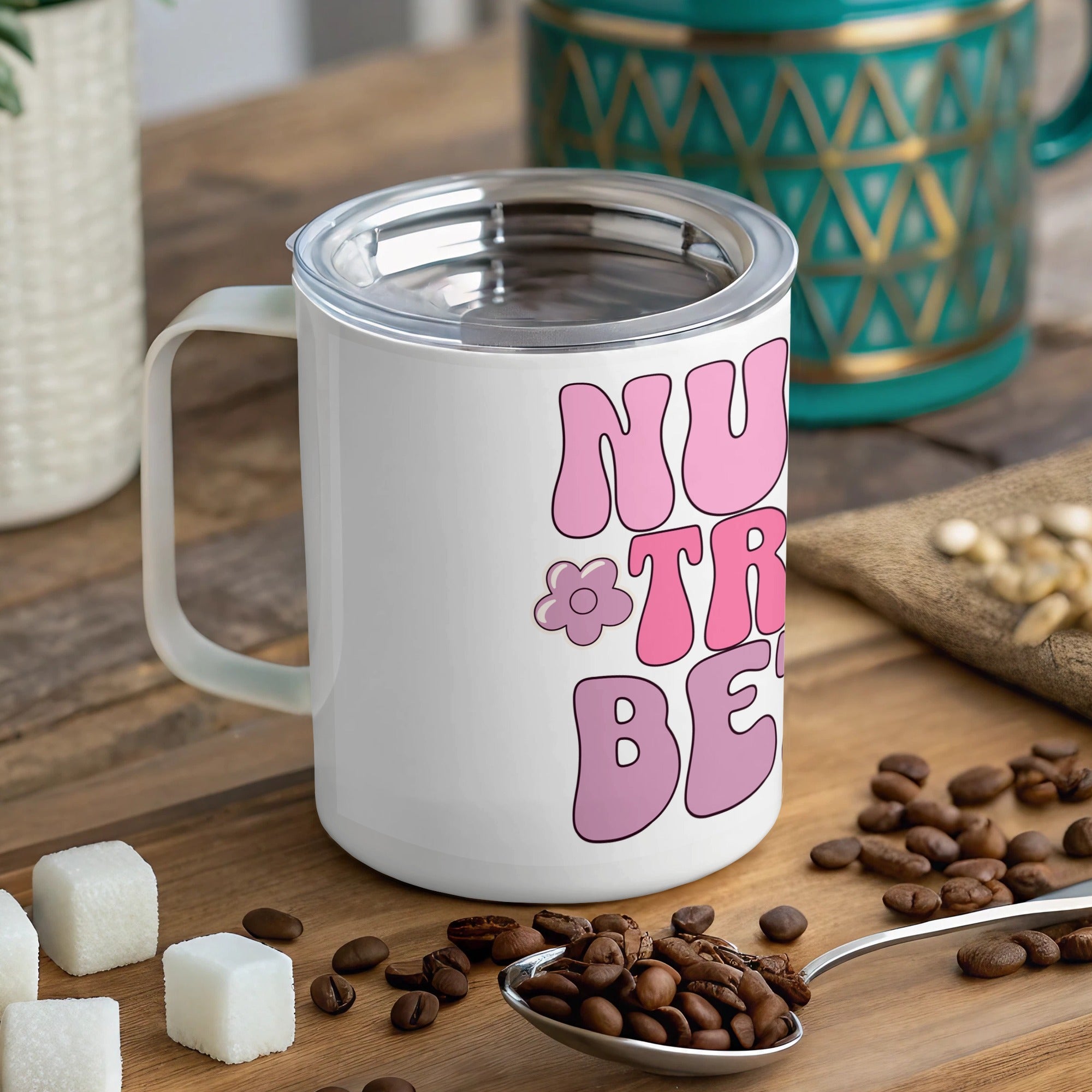 White mug with "Nurse Tribe" text and a flower, lid on, on a wooden surface.