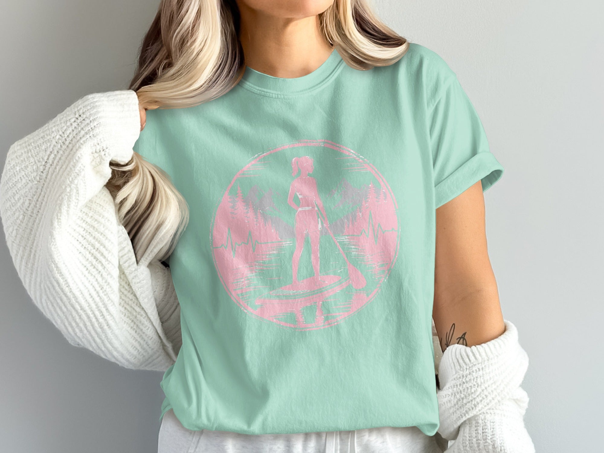 Pale pink silhouette of a woman paddleboarding inside a circle with forest background.
