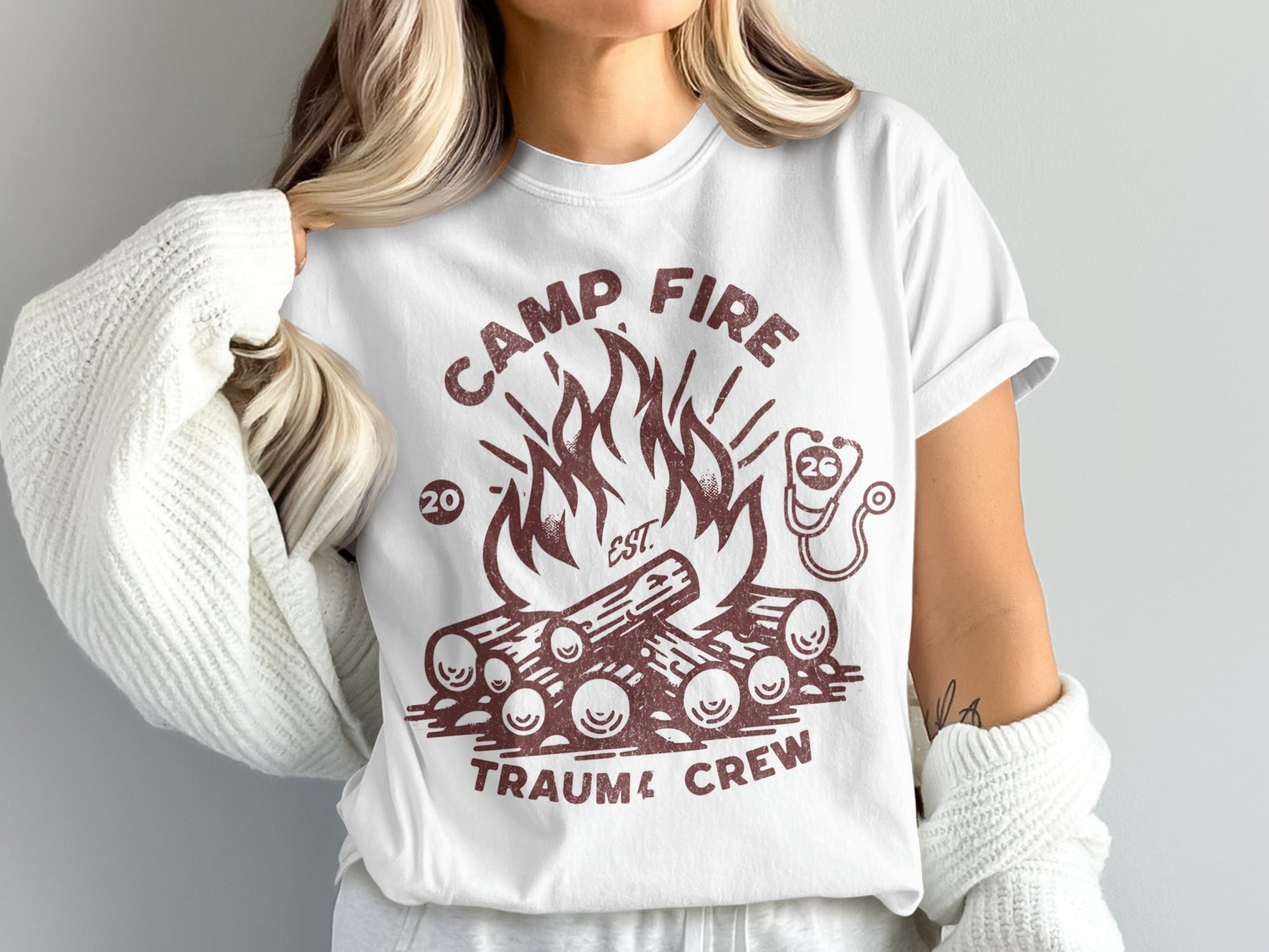 White t-shirt with a campfire graphic and text that reads "Camp Fire Trauma Crew."