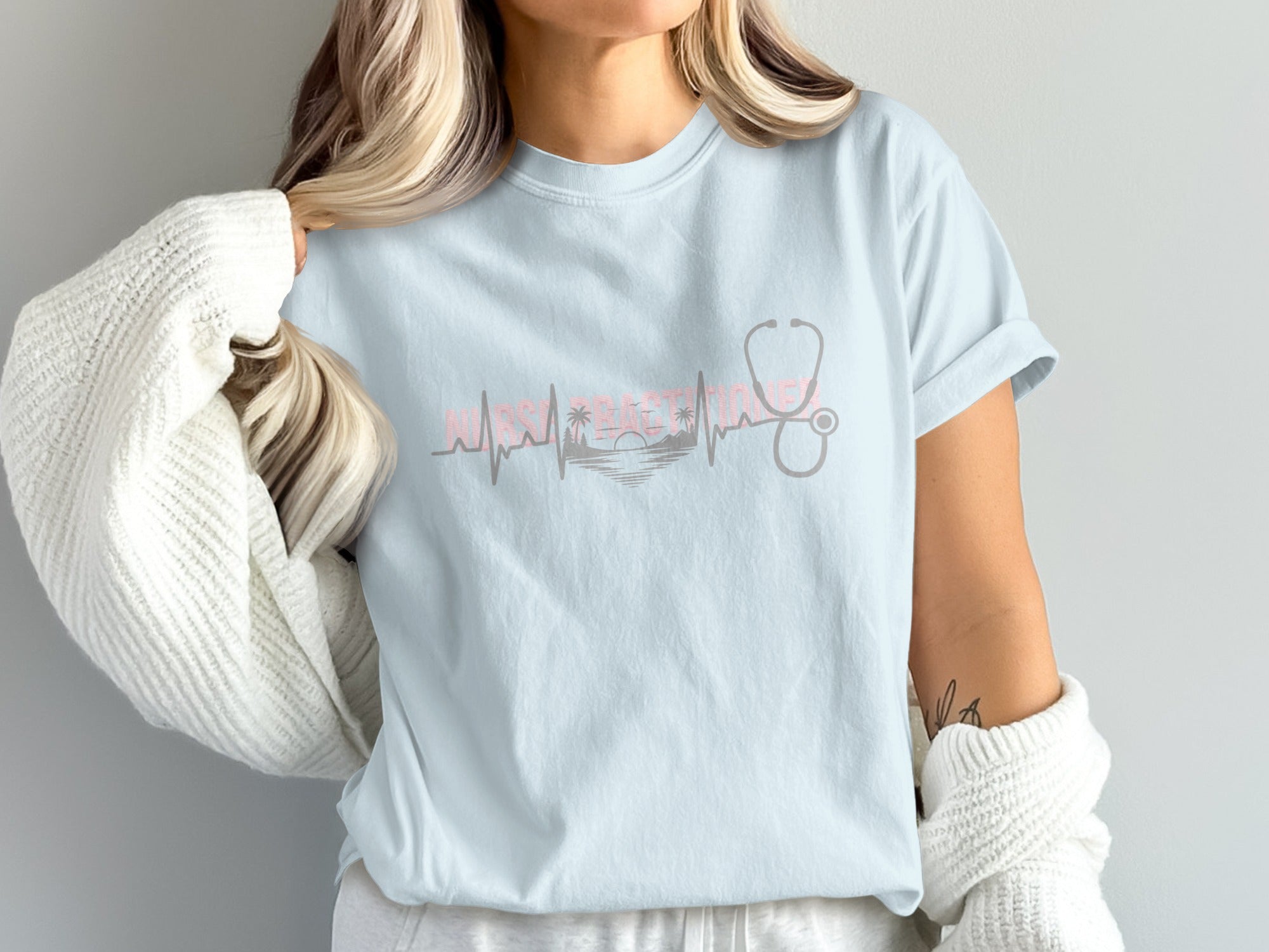 Light blue t-shirt with stethoscope pulse, sunset, and palm trees graphic.