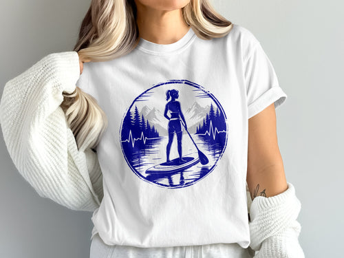 Woman on paddleboard with mountains and lake graphic on white t-shirt.