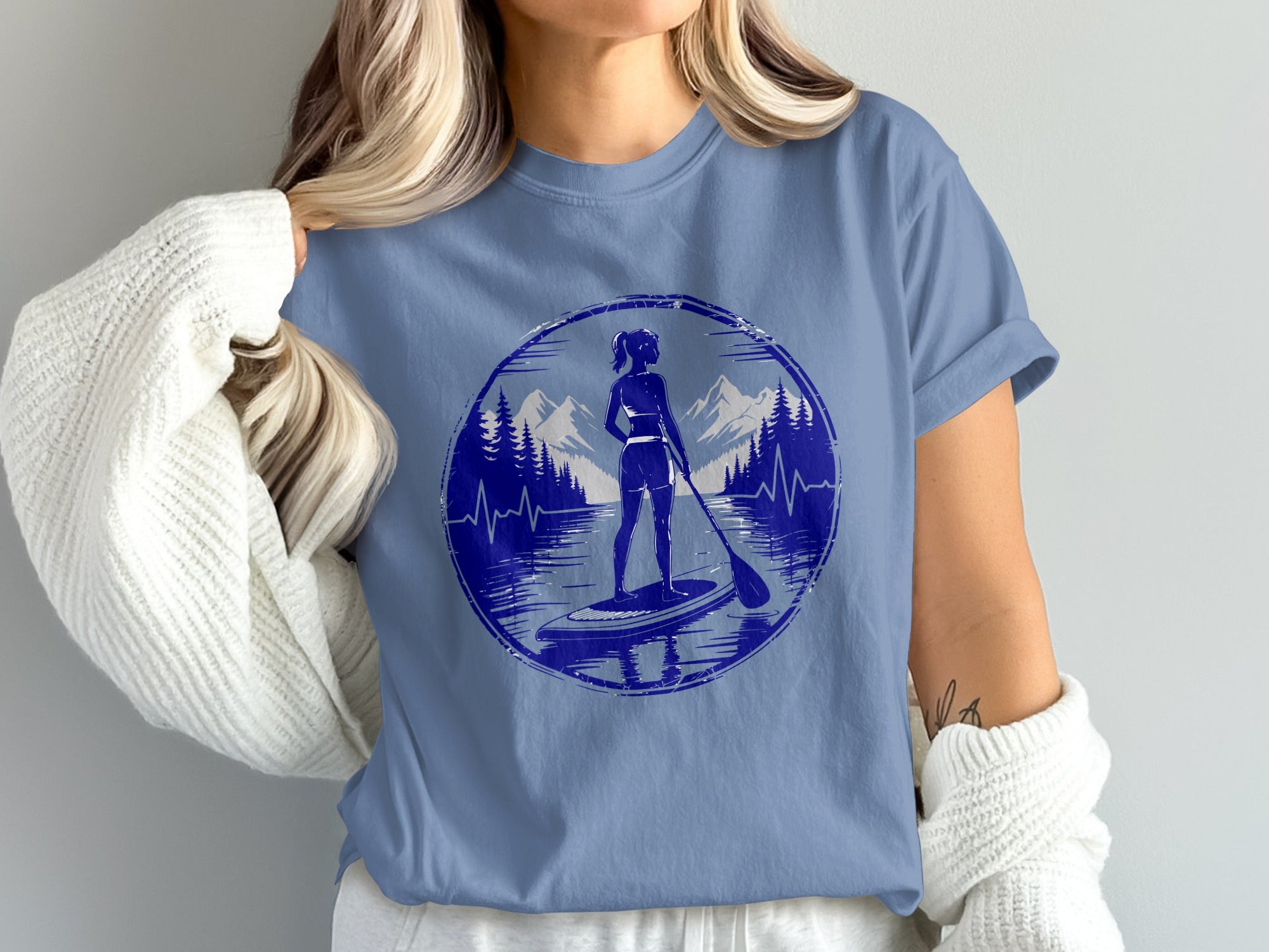 Woman wearing blue t-shirt with paddleboarder in circular mountain graphic.