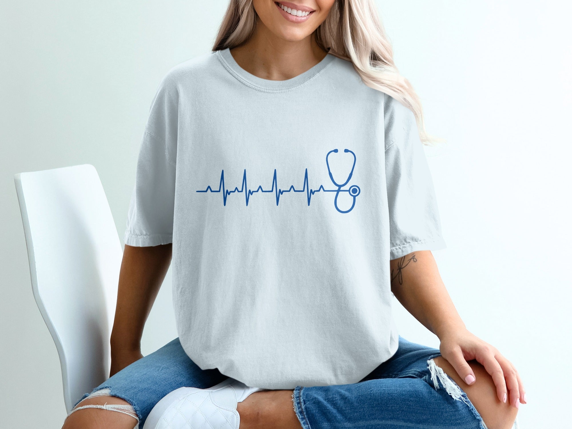 Blue stethoscope ECG line graphic on a white t-shirt worn by a person.