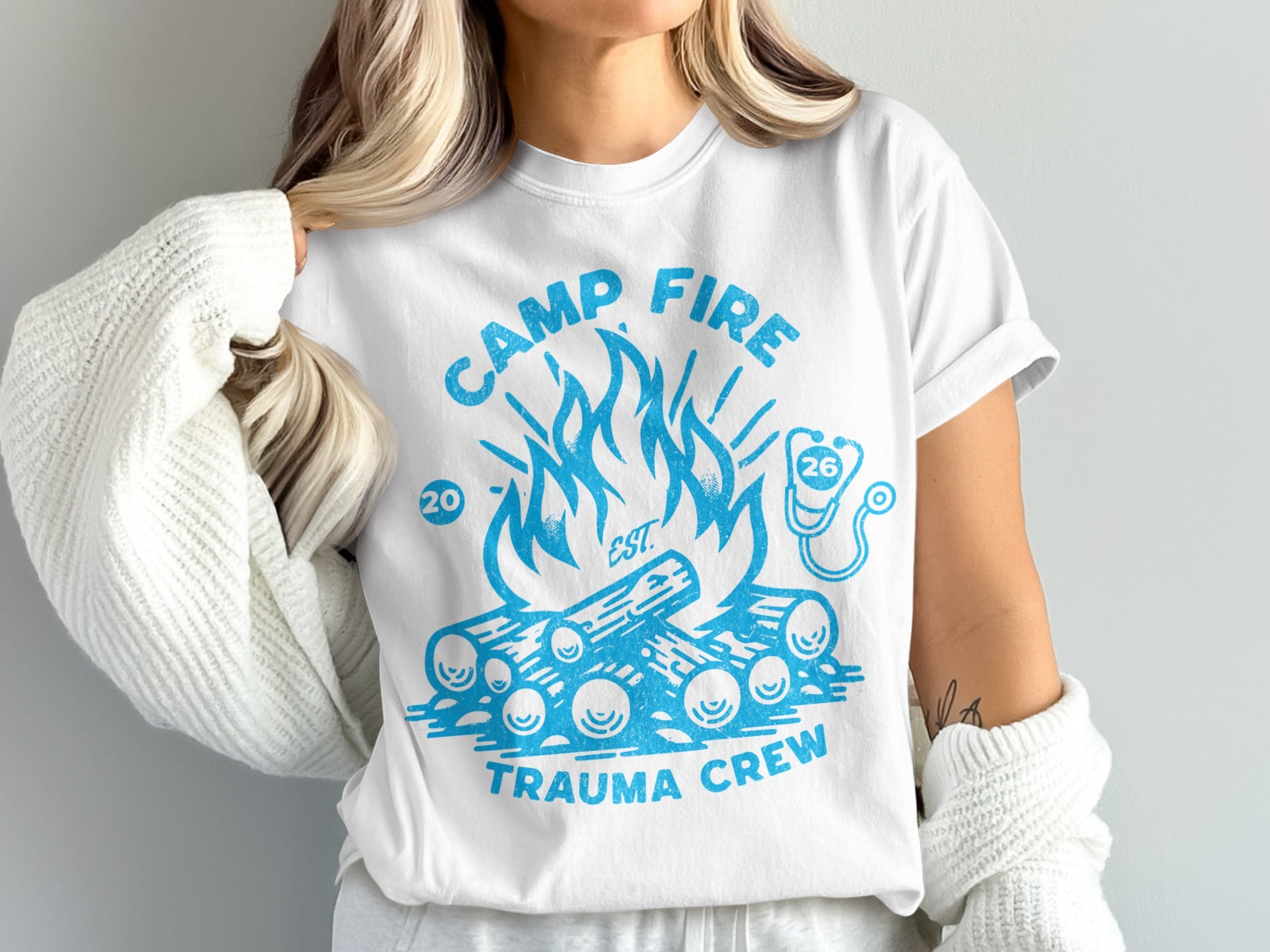 White t-shirt with blue campfire and "Trauma Crew" text.