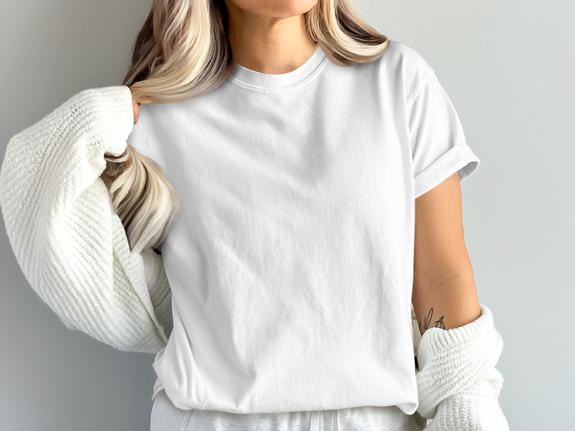 Woman wearing a plain white t-shirt and cream knit sweater.