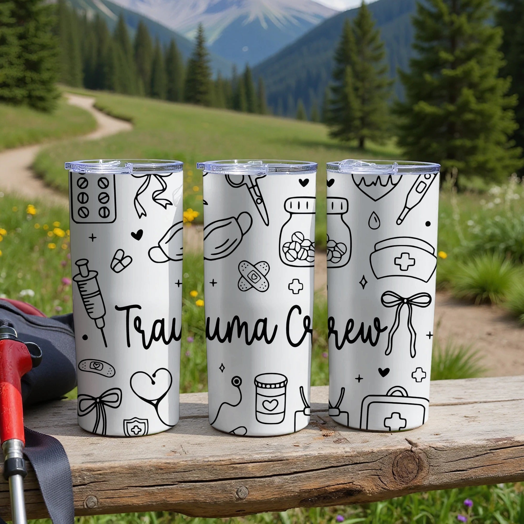 Three white tumblers with medical icons and "Trauma Crew" text on a wooden surface.