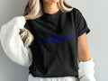 Black t-shirt with blue electrocardiogram design featuring a camper and stethoscope above "TRAVEL NURSE".