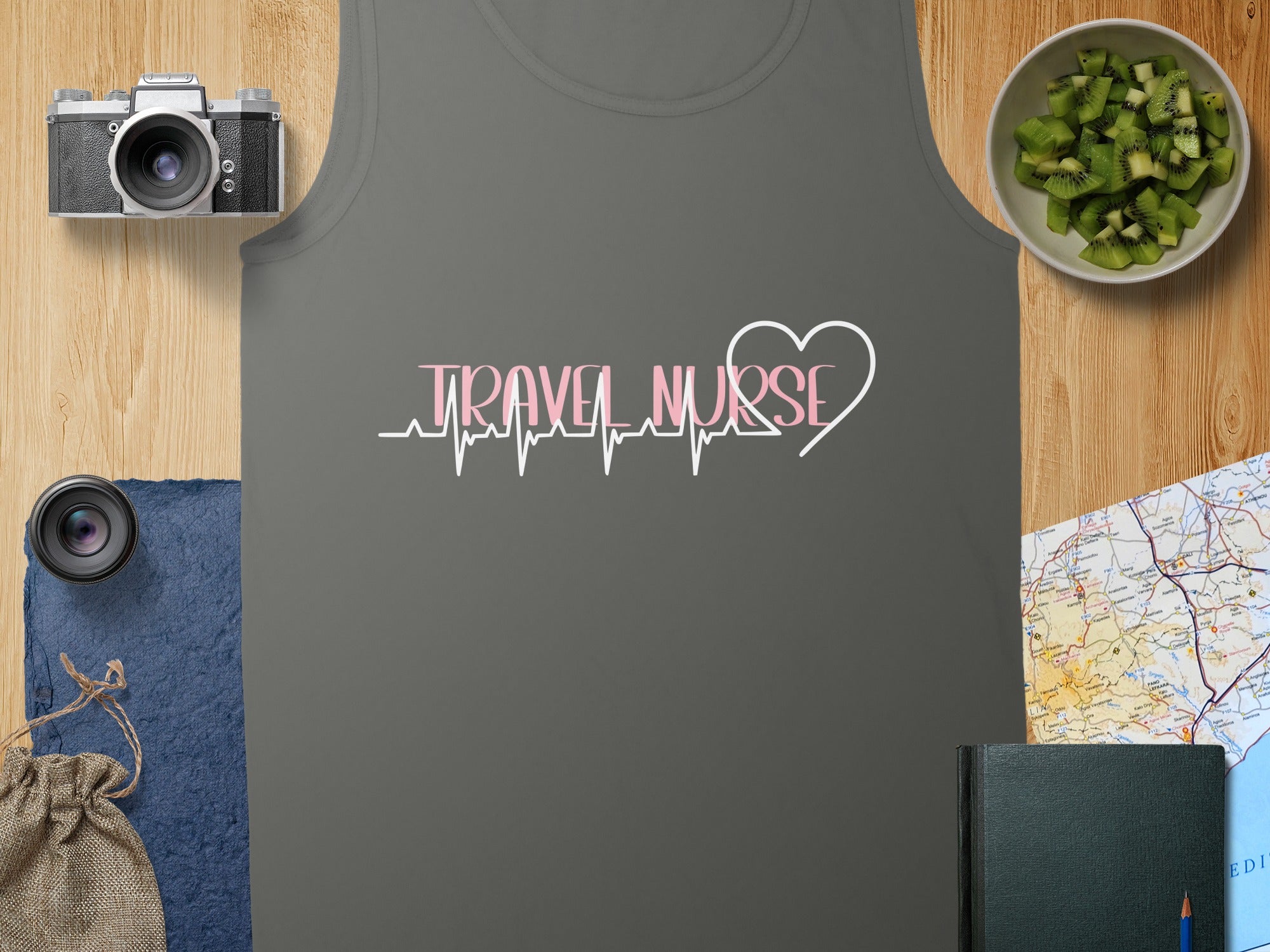Dark grey tank top with "Travel Nurse" electrocardiogram design and camera on wooden table.